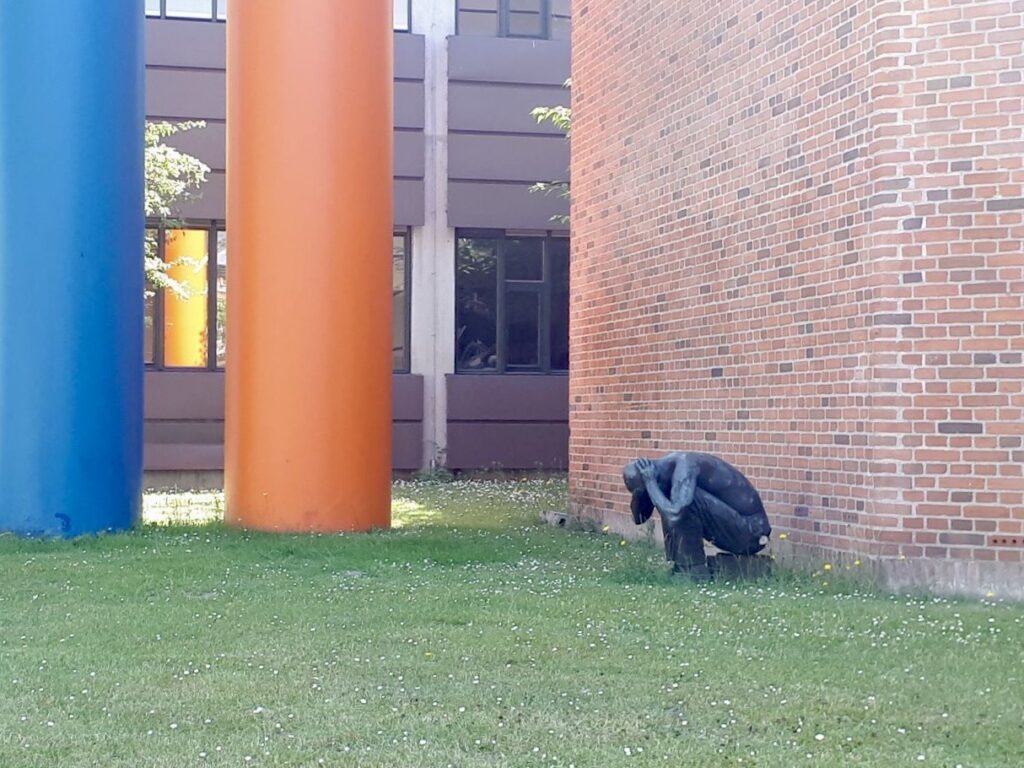 Kuva Kööpenhaminasta matkalta konferenssipaikalle. Kuvassa patsas, joka on rakennuksen seinän vieressä kyyryssä ja pitelee päätään.